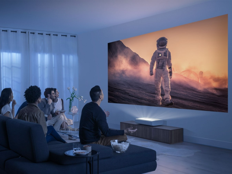 Grupa ludzi ogląda duży ekran na projektorze Samsung. Wyświetlanie astronauty na powierzchni innej planety w nowoczesnym salonie.