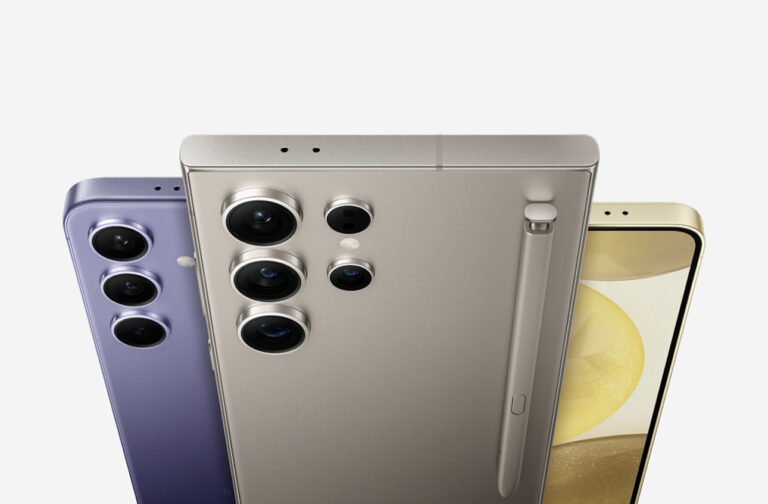 Trzy smartfony z serii Samsung Galaxy S24 ustawione obok siebie pod kątem, ukazujące ich tylne panele z potrójnymi aparatami fotograficznymi, w kolorach fioletowym, srebrnym i złotym.