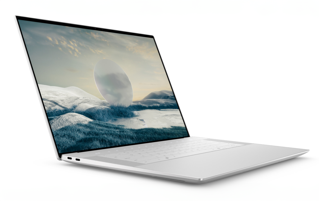 Laptop z otwartą białą klawiaturą i dużym ekranem bezramkowym, wyświetlającym obraz krajobrazu zimowego o zachodzie słońca.