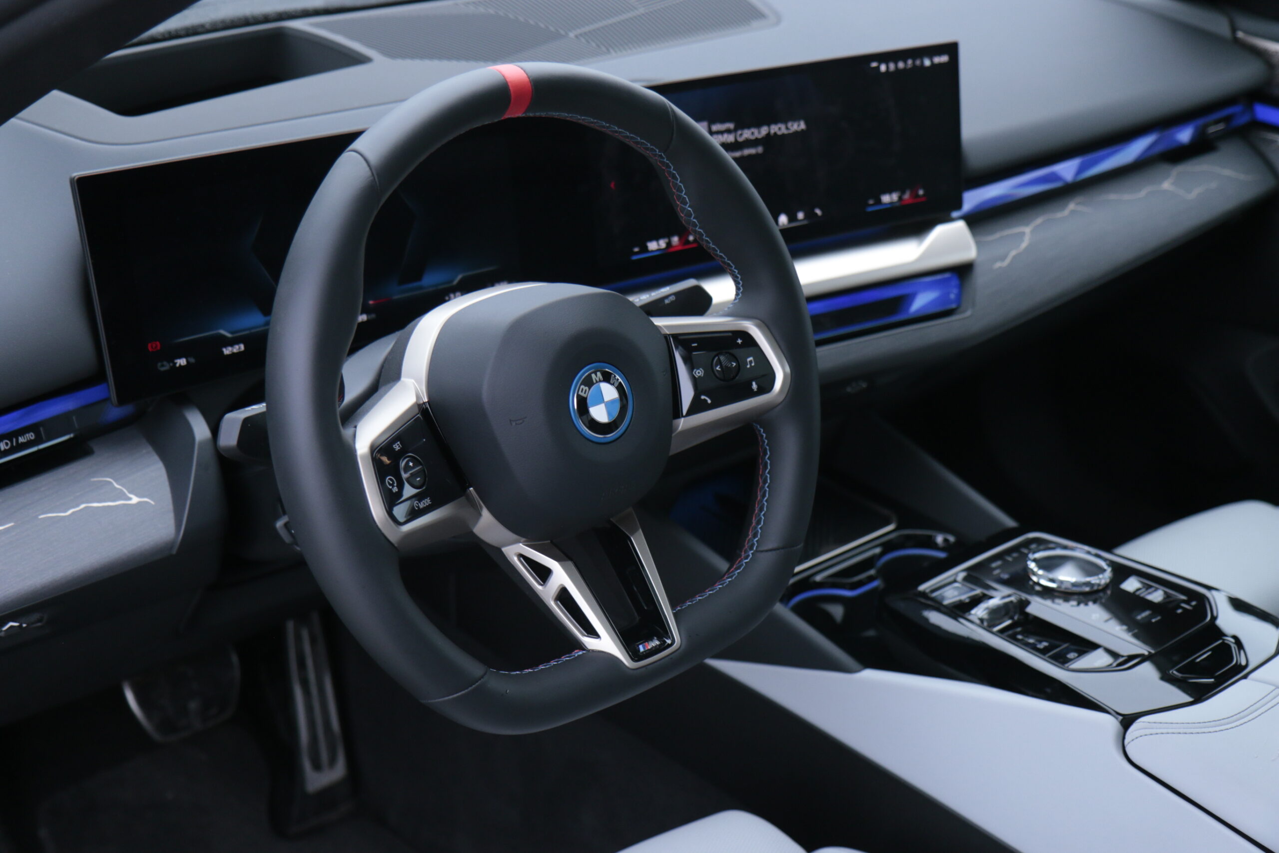 Wnętrze testowanego BMW i5 M60 xDrive z widoczna kierownicą, deską rozdzielczą z ekranami multimedialnymi i centralnym panelem sterowania.
