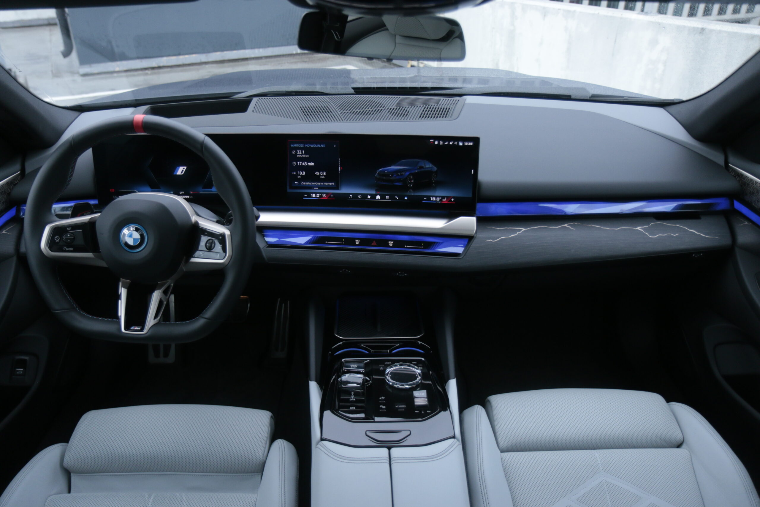 Wnętrze testowanego BMW i5 M60 xDrive z widokiem na kierownicę, ekran systemu multimedialnego i centralną konsolę.