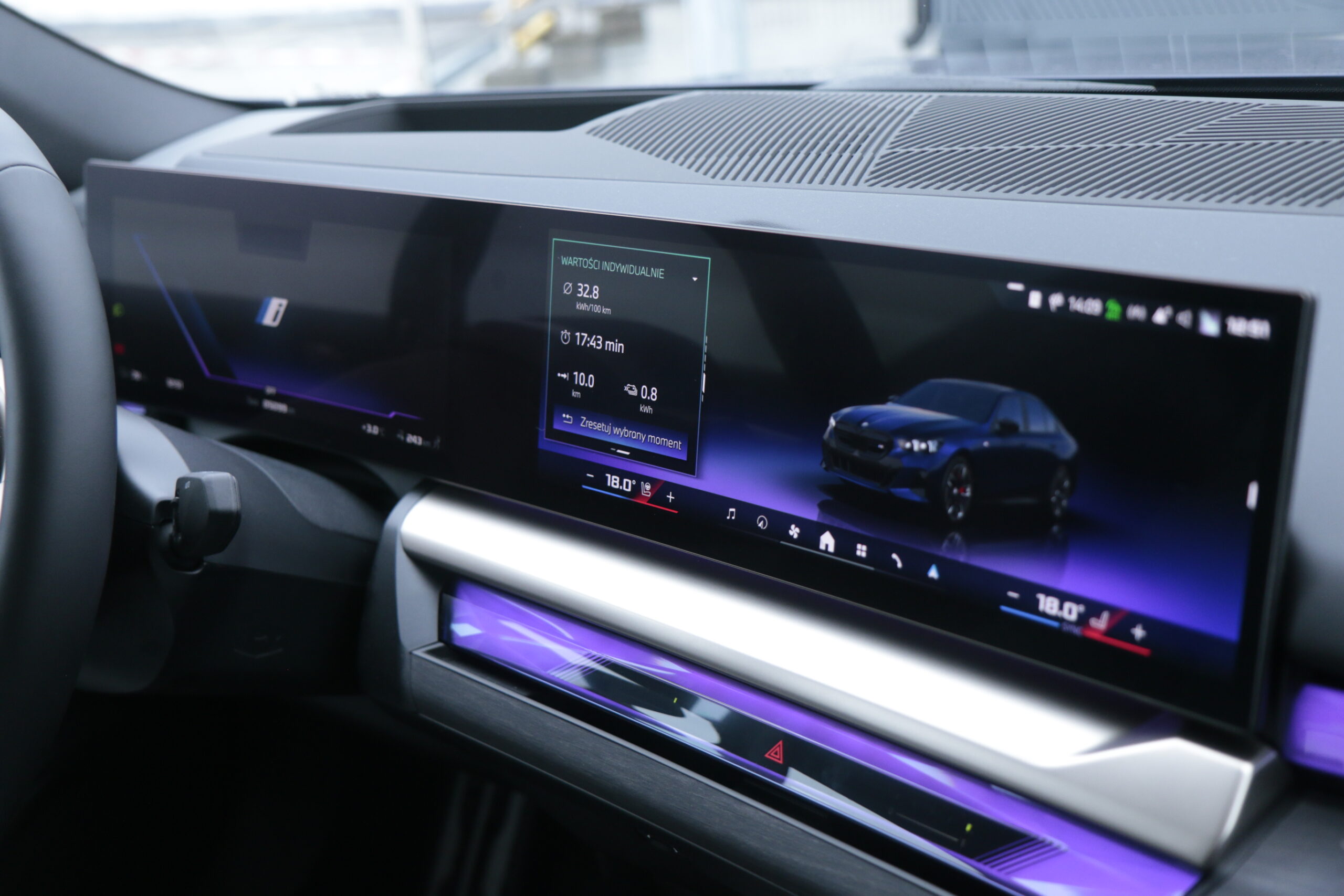 Wnętrze testowanego BMW i5 z widokiem na cyfrowy wyświetlacz deski rozdzielczej pokazujący informacje o pojeździe i multimedia.