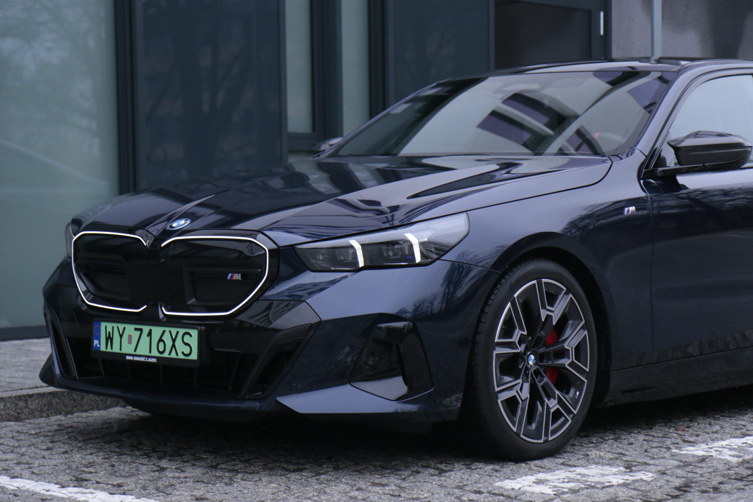 Czarny samochód BMW serii M zaparkowany na ulicy, z widocznym przednim kołem i częścią maski.