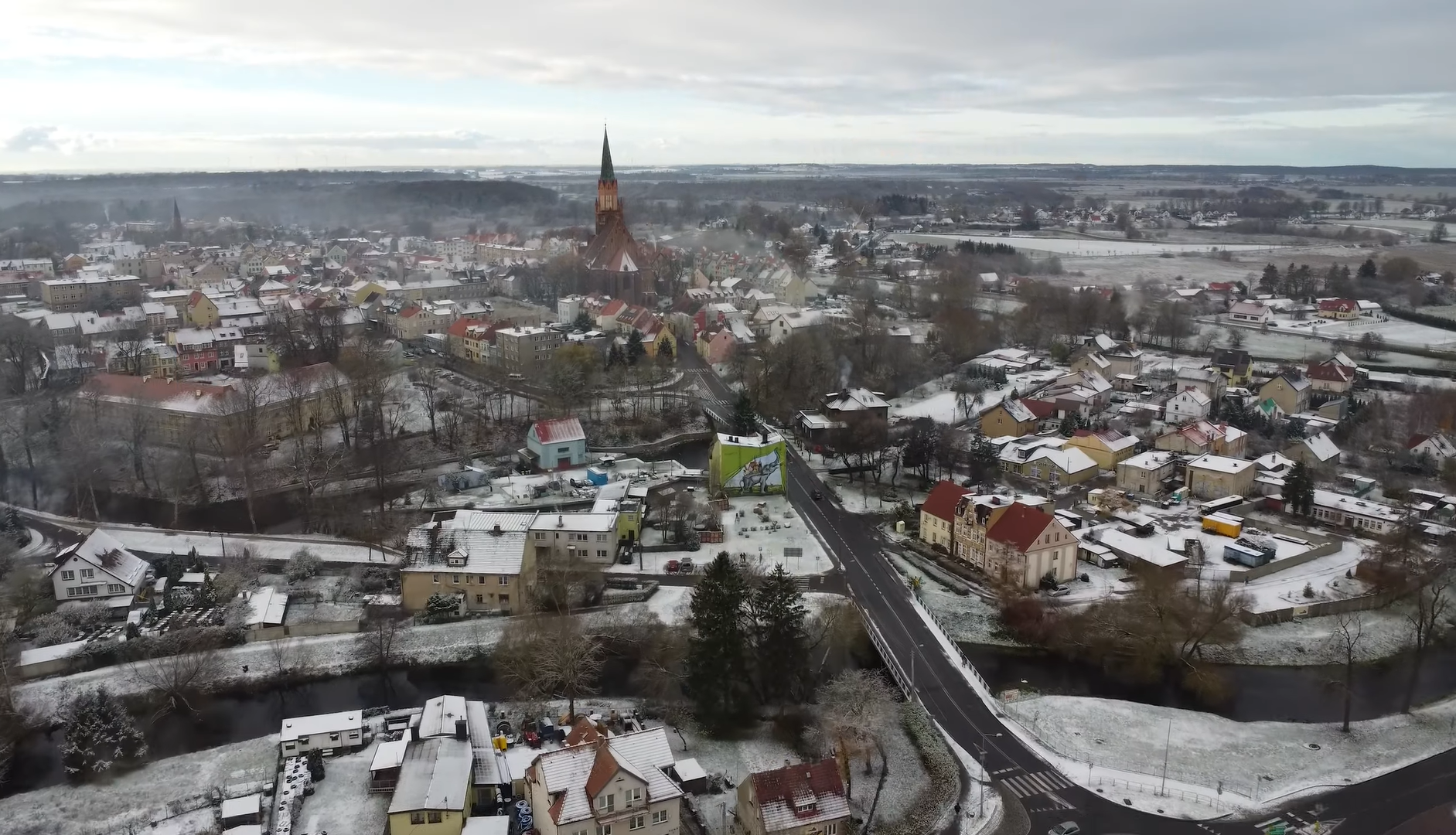 Widok z lotu ptaka na zimowe miasteczko Trzebiatów z kościołem o wysokim, strzelistym dachu, domami z kolorowymi fasadami i drogami pokrytymi częściowo śniegiem.