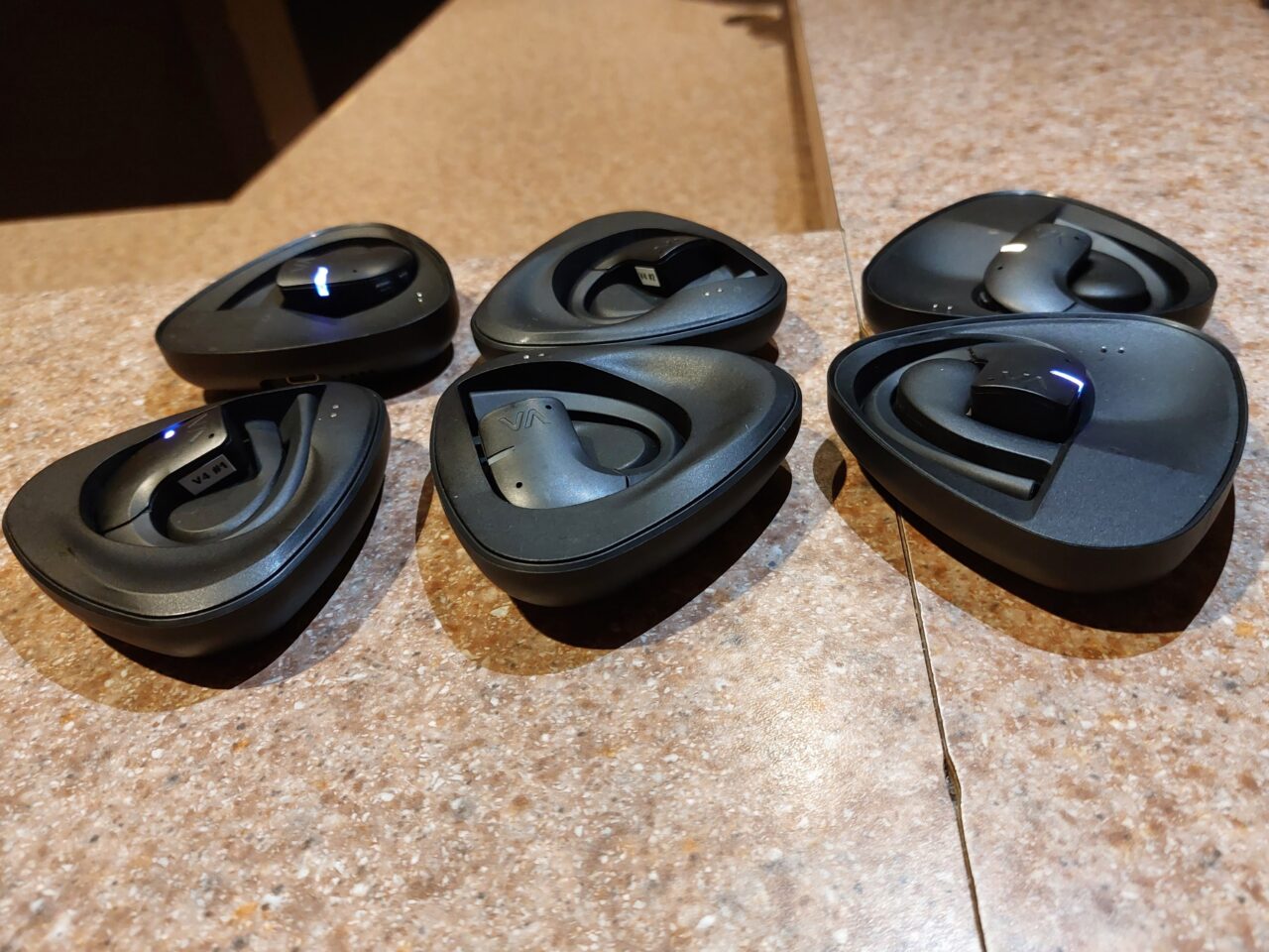 Cztery czarne, otwarte etui do słuchawek bezprzewodowych ułożone na kamiennym blacie.