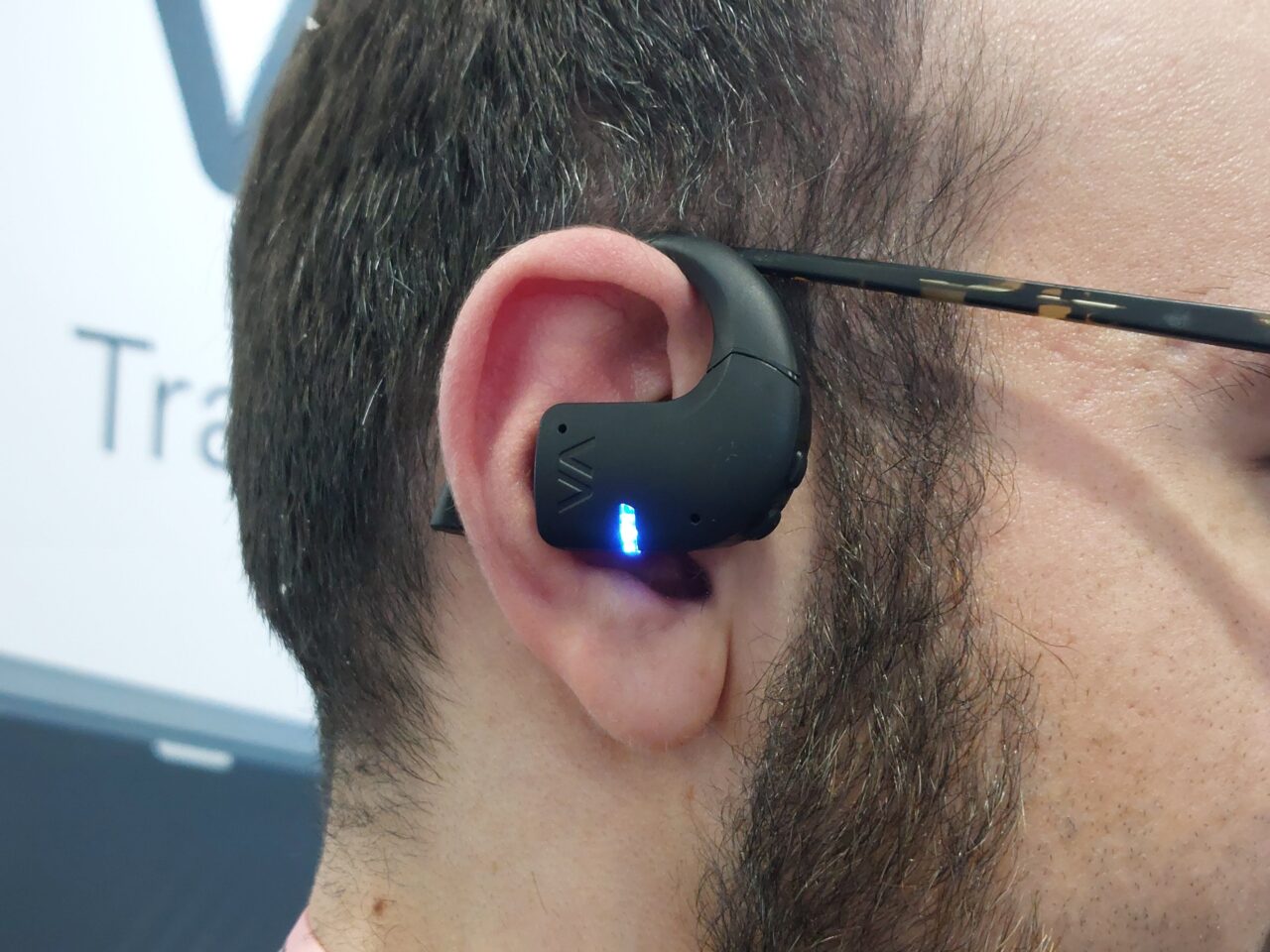 Mężczyzna z czarnym bezprzewodowym słuchawkiem w uchu, na słuchawce świeci się niebieska dioda.