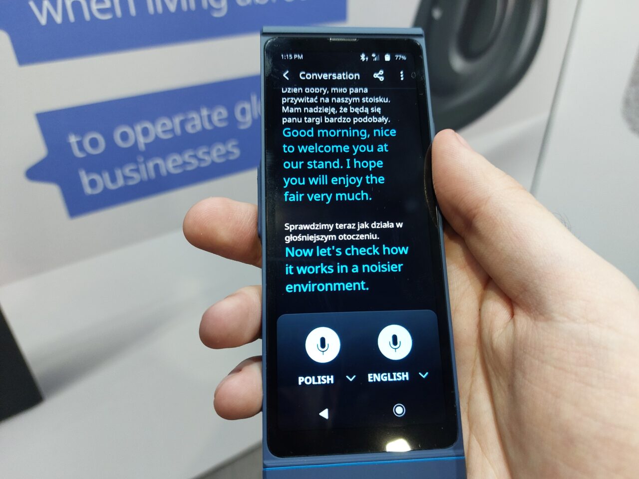 Osoba trzyma smartfon wyświetlający aplikację do tłumaczenia z polskiego na angielski z widocznym tekstem rozmowy.