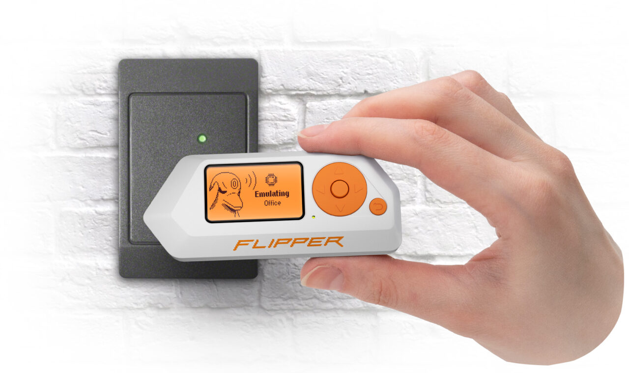 Urządzenie Flipper Zero do kontroli dostępu typu "flipper" trzymane w dłoni przed czytnikiem kart na białej ścianie.