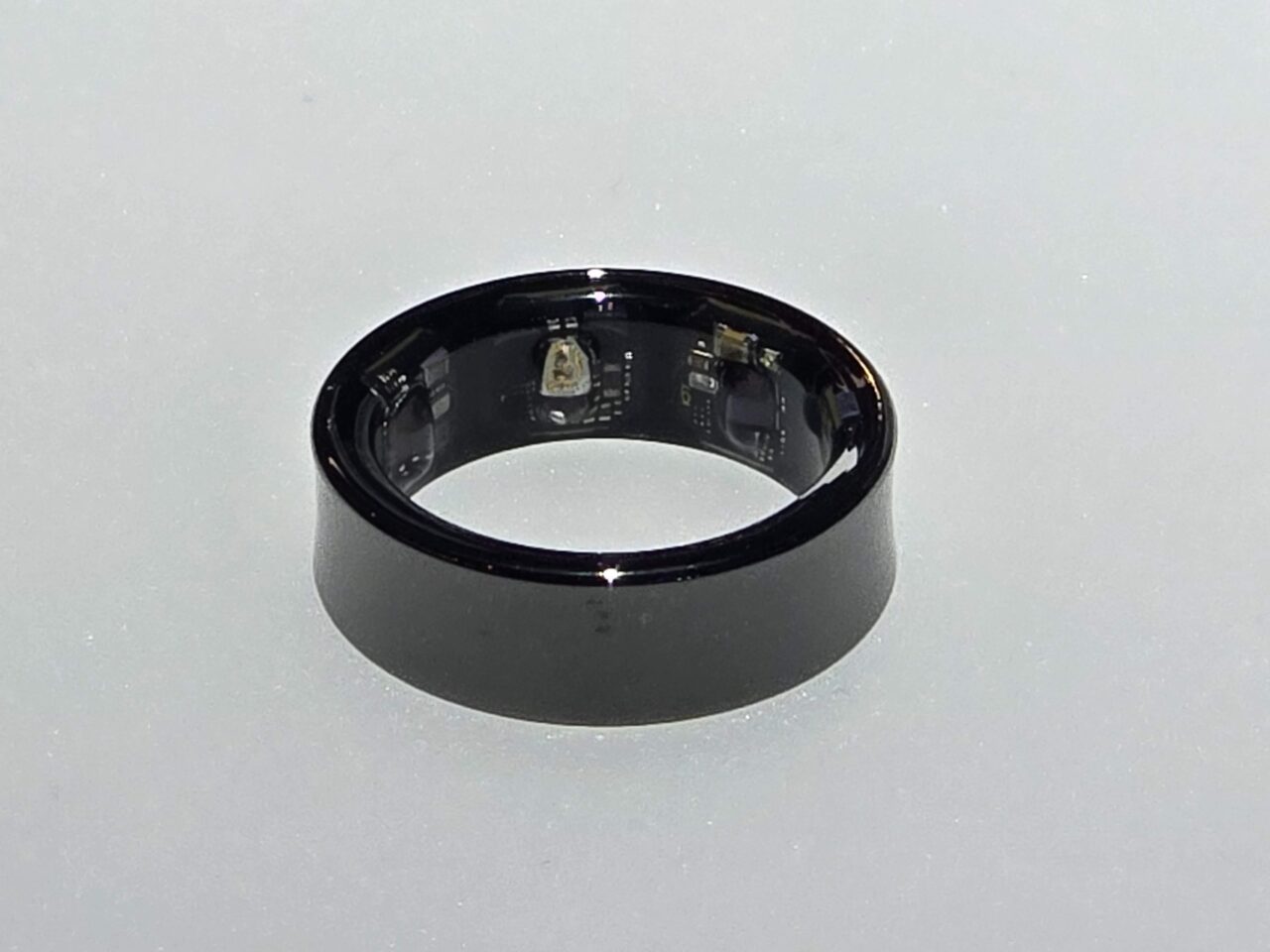 Czarny Samsung Galaxy Ring z widocznymi elementami elektronicznymi wewnątrz, położona na jasnej powierzchni.