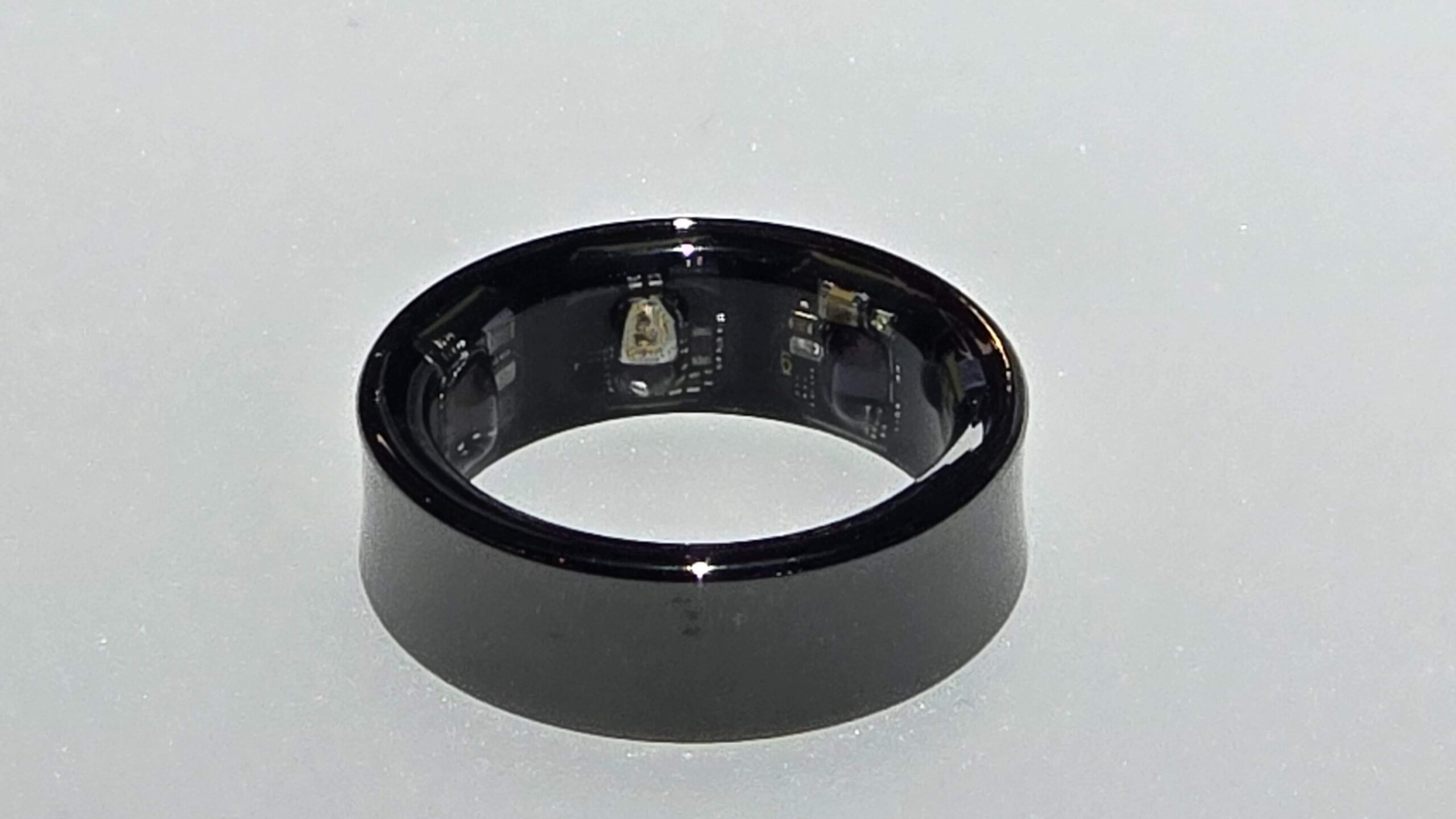 Czarny Samsung Galaxy Ring z widocznymi elementami elektronicznymi wewnątrz, położona na jasnej powierzchni.