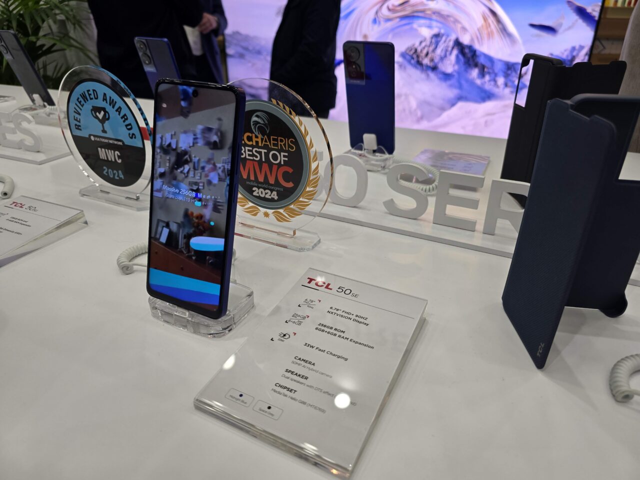 Smartfony wystawione na stoisku, jeden z nich z ekranem skierowanym do przodu, z nagrodami w tle i specyfikacją techniczną na dole.