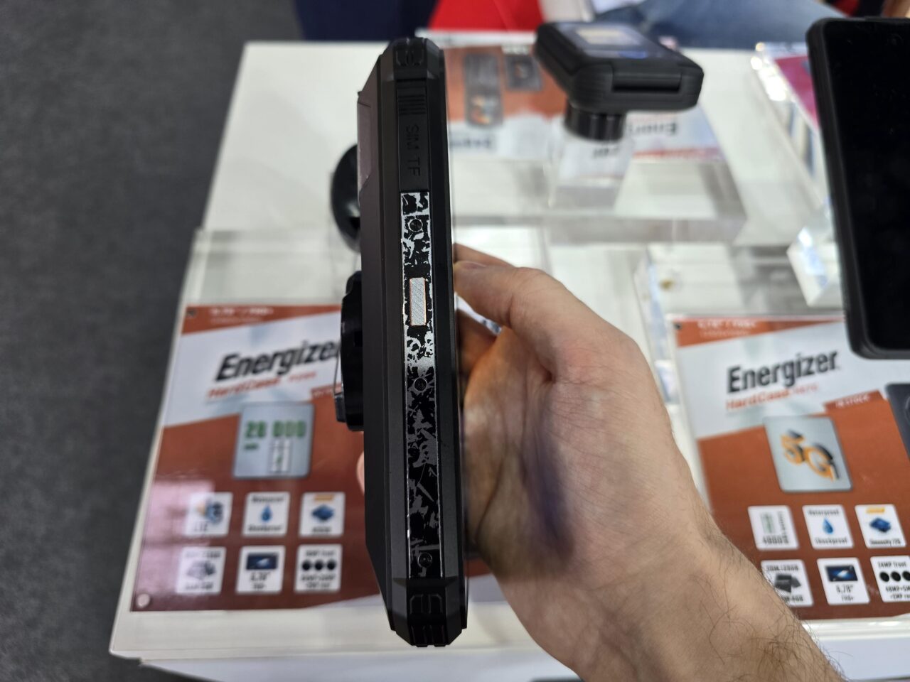Dłoń trzymająca czarny smartfon Energizer Hard Case P28K przed wystawką z innymi produktami marki Energizer.