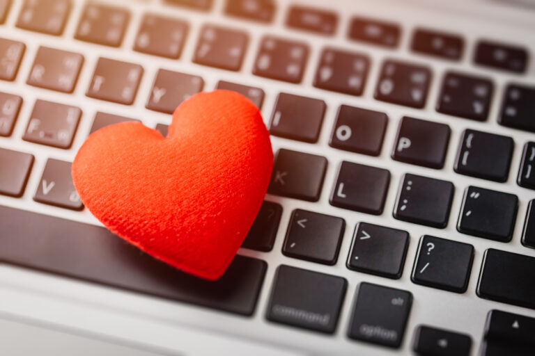 Czerwone pluszowe serce leżące na klawiaturze laptopa.