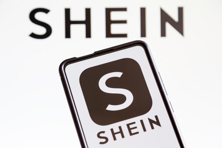 Smartfon z logo aplikacji SHEIN na ekranie, umieszczony na tle z nieostrym logo SHEIN.