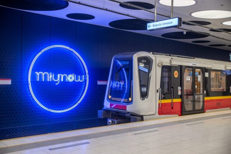 Metro Warszawa. Pociąg na stacji metra Młynów z wyświetloną nazwą stacji w formie niebieskiego neonu na ścianie.