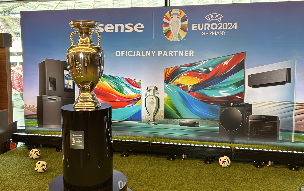 Ekspozycja reklamowa z pucharem na podium, logo UEFA EURO 2024 i produktami Hisense, z oficjalnym partnerstwem w tle.