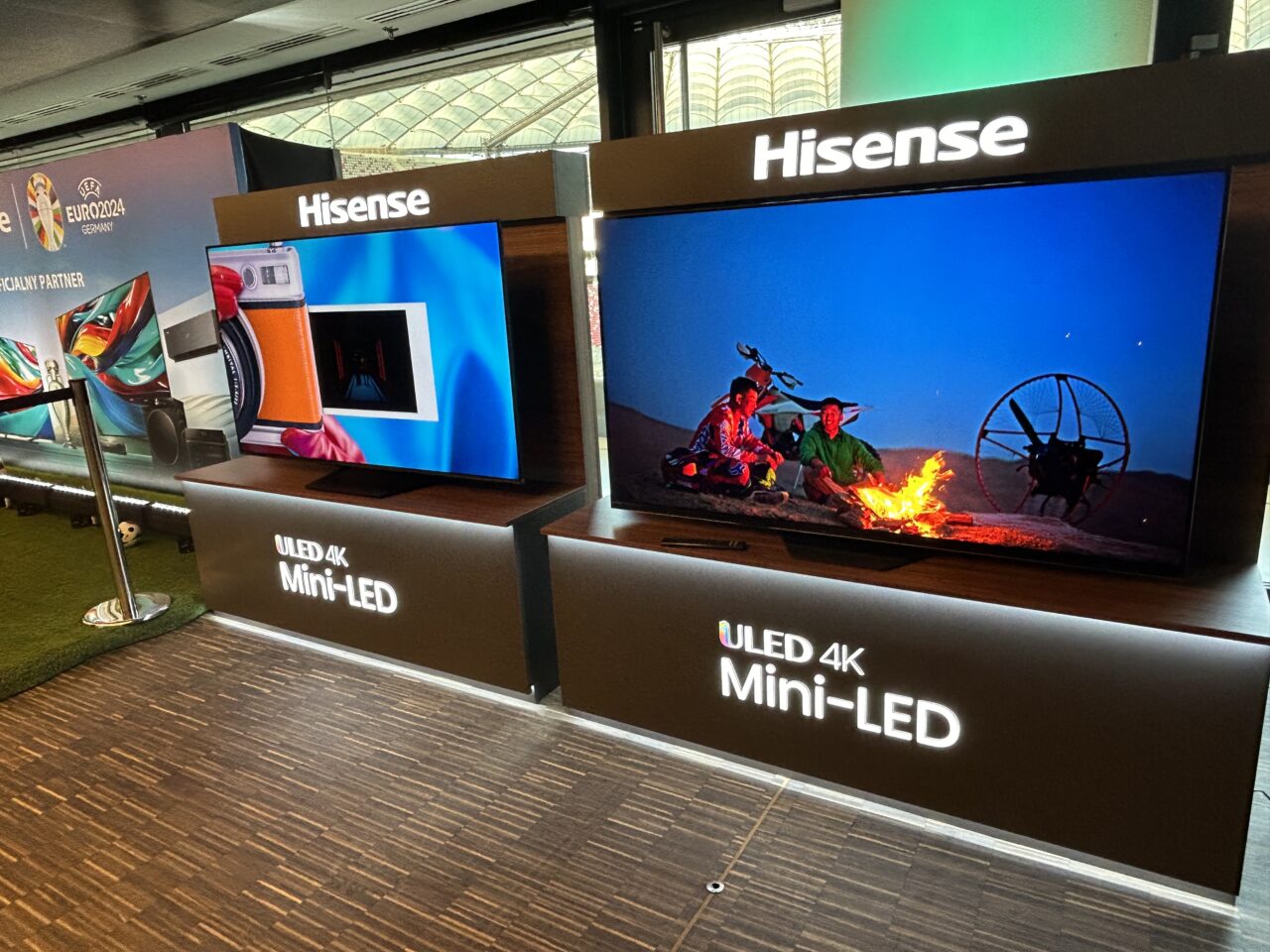 Stoisko z telewizorami marki Hisense, przedstawiające modele ULED 4K Mini-LED z wyświetlanymi kolorowymi obrazami, w tle widoczne plakaty promocyjne UEFA Euro 2024.