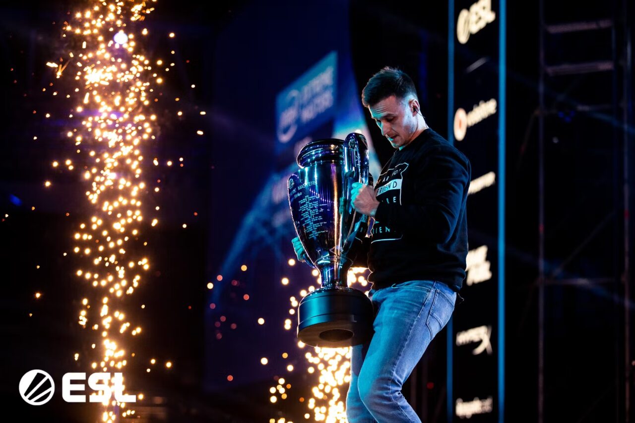 Mężczyzna trzymający puchar zwycięzcy na scenie z fajerwerkami w tle na wydarzeniu ESL.