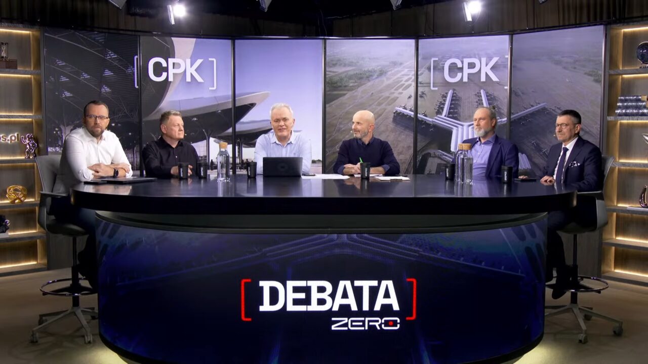 Debata CPK w Kanał Zero. Sześciu mężczyzn siedzi przy okrągłym stole podczas telewizyjnej debaty z napisem "DEBATA ZERO" na pierwszym planie oraz grafikami przedstawiającymi plany lotniska oznaczone logiem "CPK" w tle.