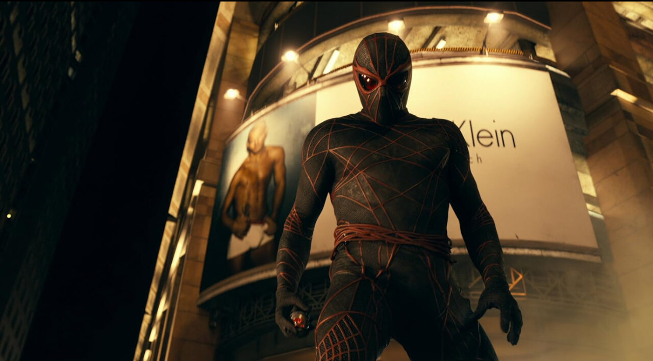 Antagonista z filmu Madame Web - Postać w kostiumie przypominającym pająka stoi na tle miejskiej nocnej sceny z bilbordem Calvin Klein w tle.