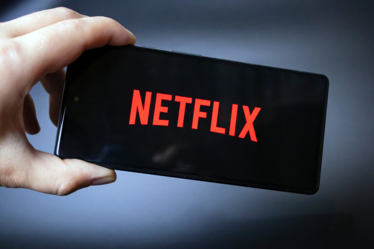 Ręka trzymająca smartfon z wyświetlonym czerwonym logo Netflix na czarnym tle.