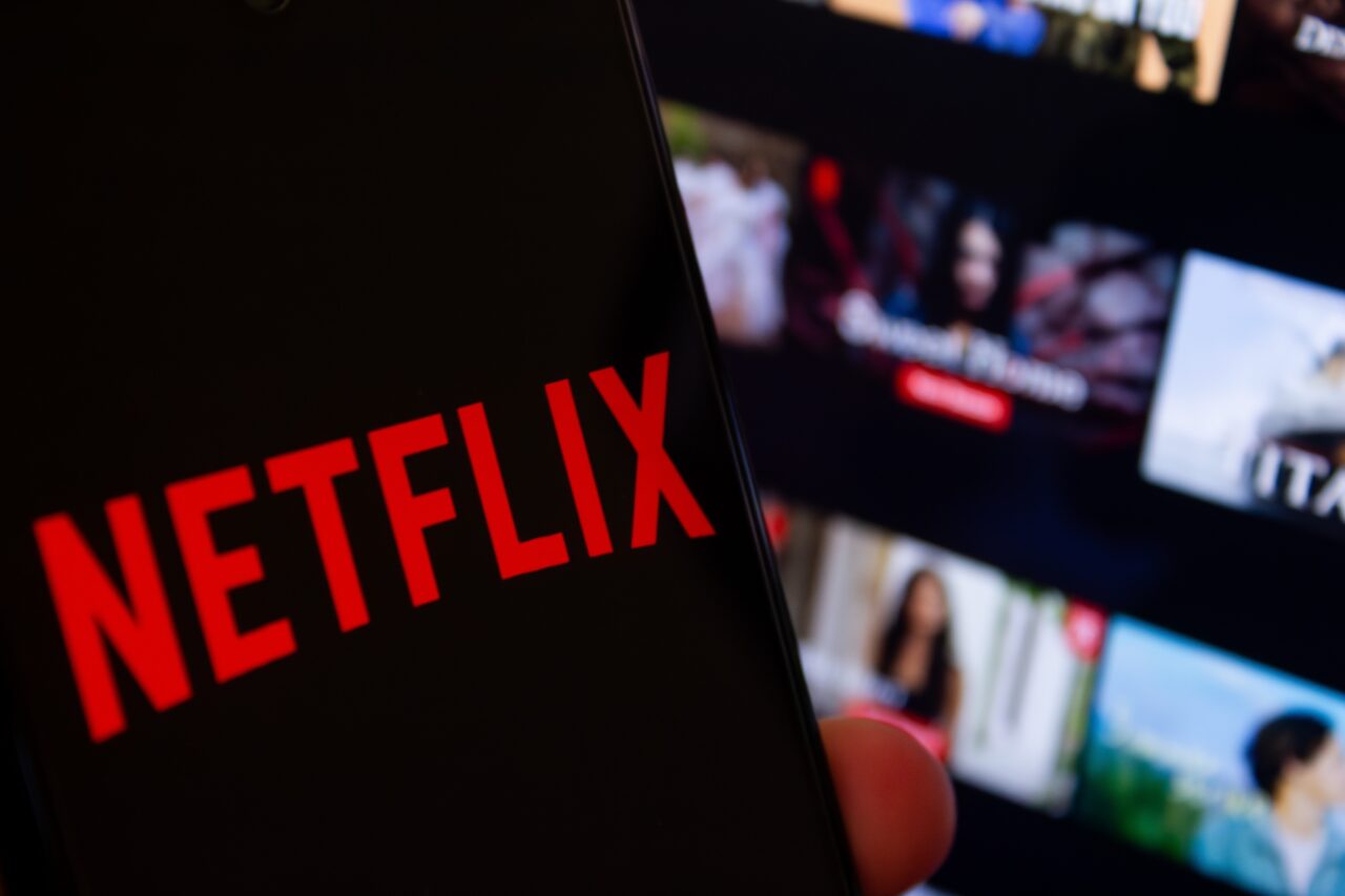 Logo Netflix na ekranie telefonu z interfejsem aplikacji w tle.