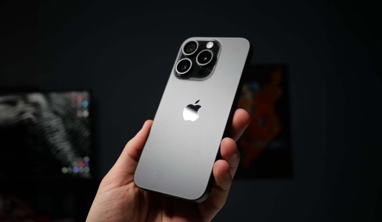 iPhone 16 plotki. Tył smartfona z logo Apple trzymanego w ręce na tle rozmytego pokoju. Smartfon dostanie aktualizację do iOS 18