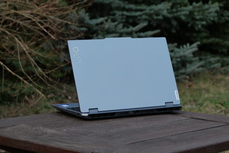 Laptop Lenovo LOQ 15 2024 umieszczony na drewnianym stole na zewnątrz, z roślinnością w tle.
