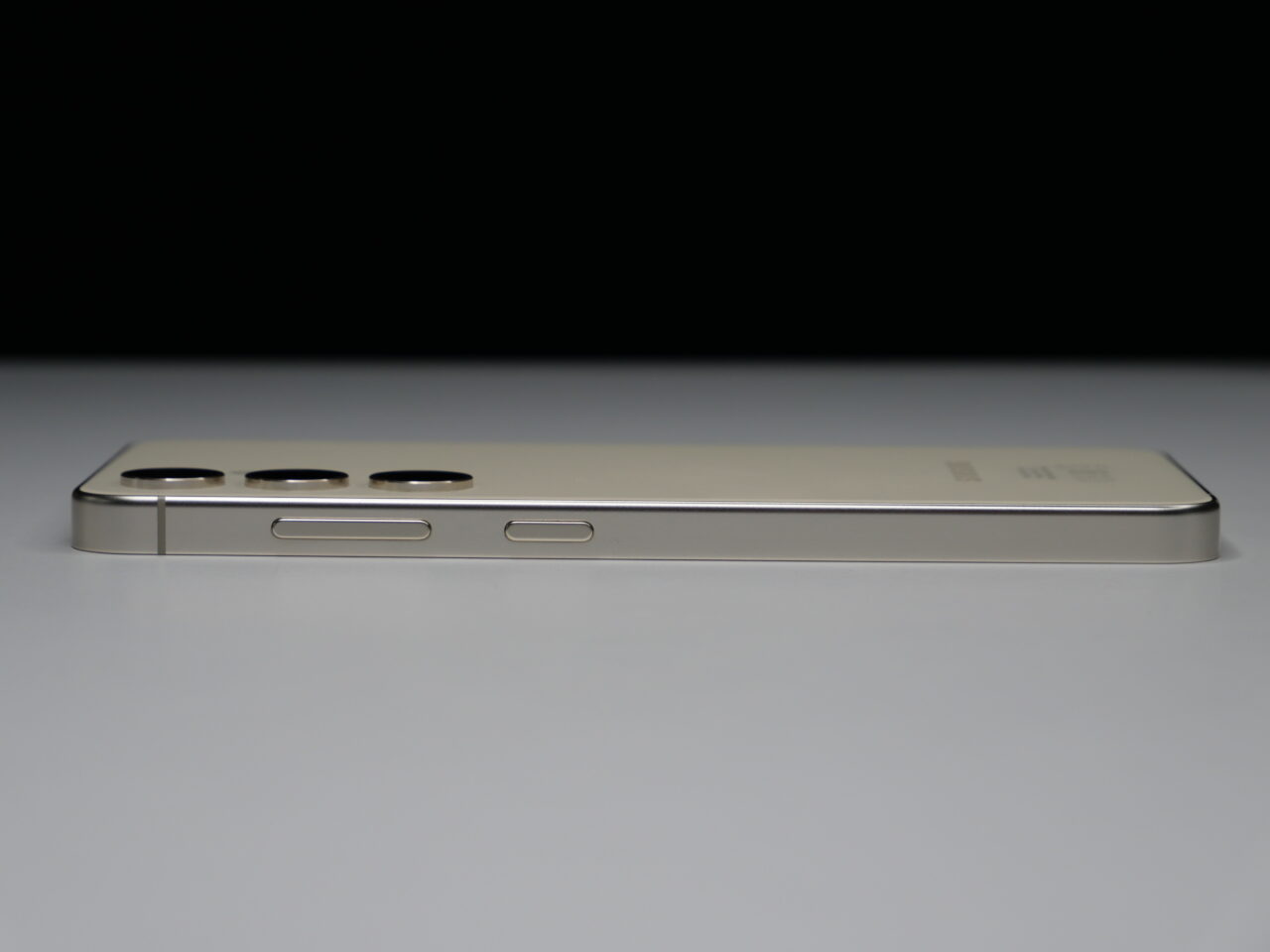 Złoty smartfon leżący na boku z widocznymi przyciskami głośności i przełącznikiem wyciszenia na białym tle.