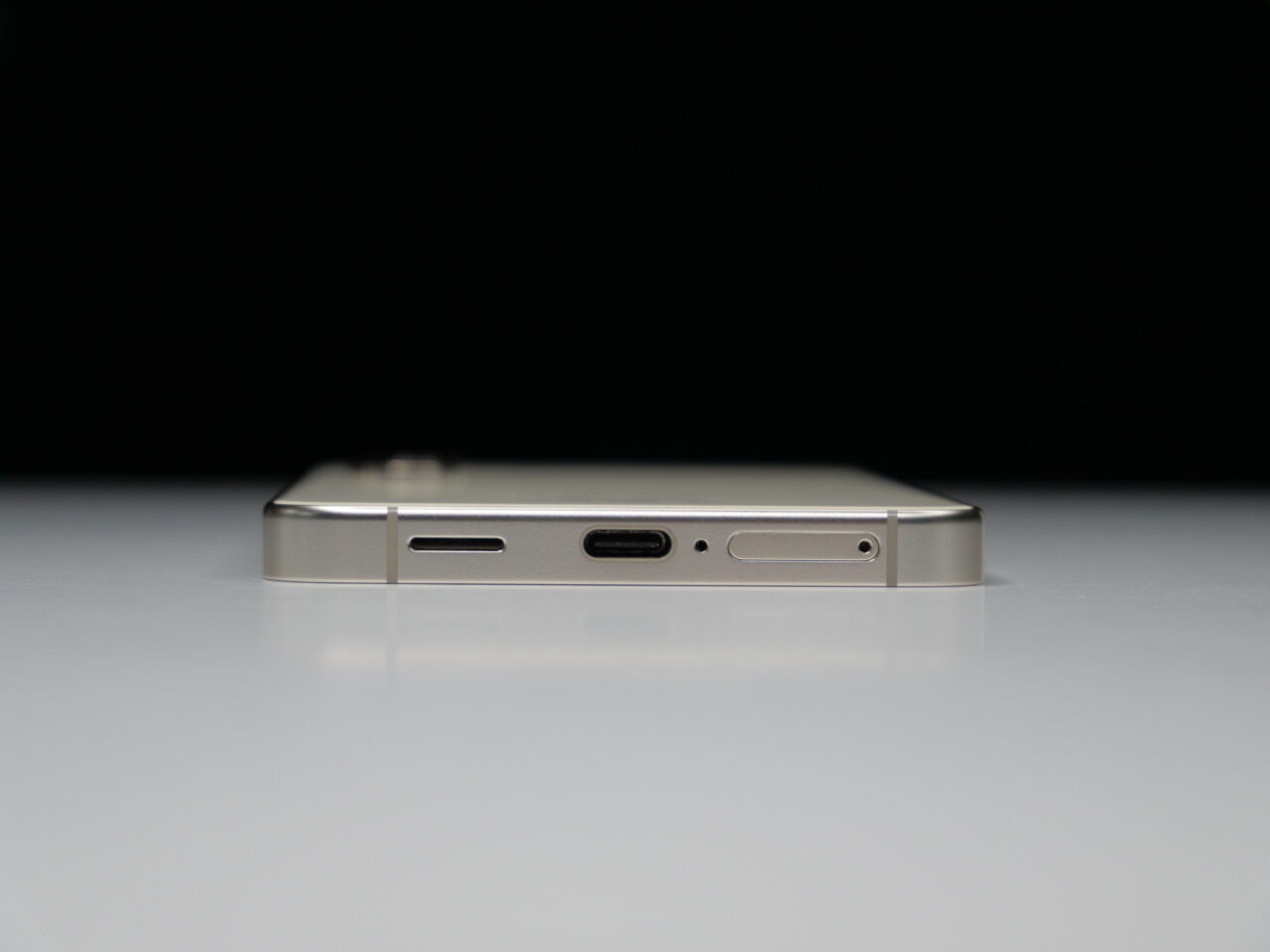 Smartfon w poziomym ustawieniu z widocznym bocznym przyciskiem i portami, umieszczony na białej powierzchni na tle czarnego tła.