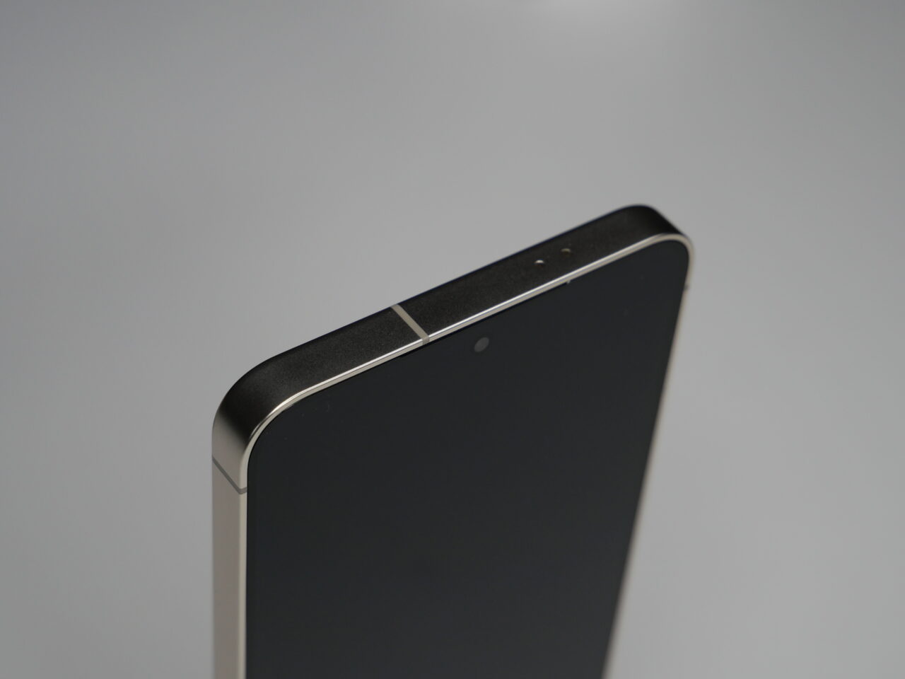 Zbliżenie na górny fragment czarnego smartfona z widocznym aparatem i głośnikiem na metalowej obudowie.