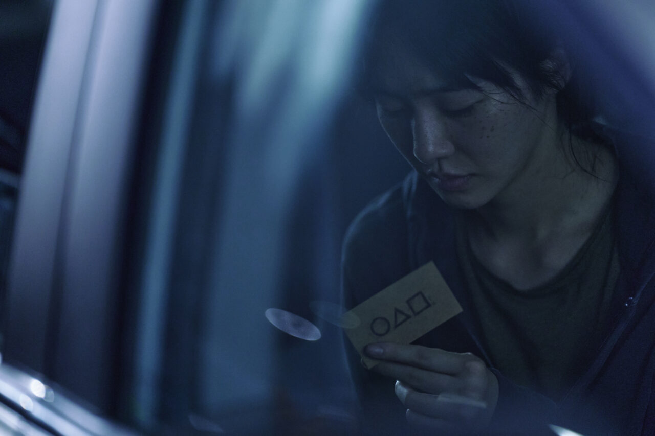 Drugi sezon Squid Game. Kobieta w ciemnym wnętrzu pojazdu trzymająca w ręku kartkę z kodem.