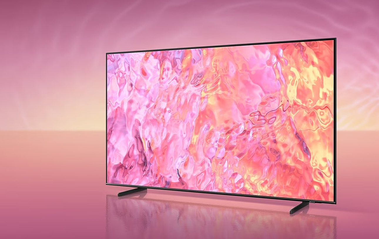 Telewizor Samsung QLED na tle o różowych odcieniach wyświetlający dynamiczne abstrakcyjne grafiki w różowym i pomarańczowym kolorze.