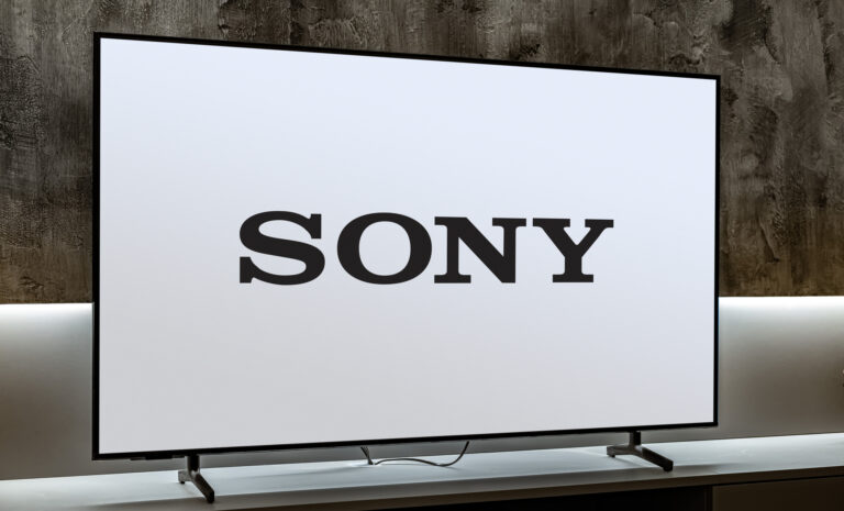 Telewizor Sony umieszczony na białym stoliku, z dużym logo Sony na ekranie, na tle ściany z ciemnego drewna.