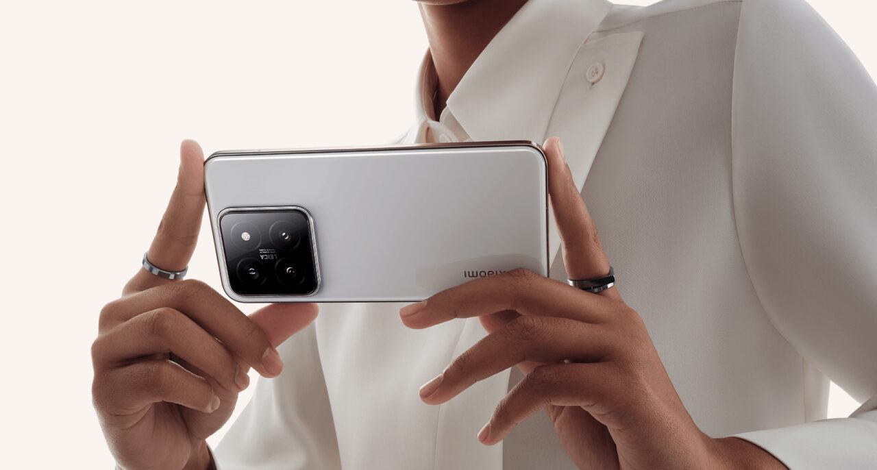 Osoba w białej koszuli trzymająca w dłoniach telefon Xiaomi 14 z widocznym aparatem z trzema obiektywami.