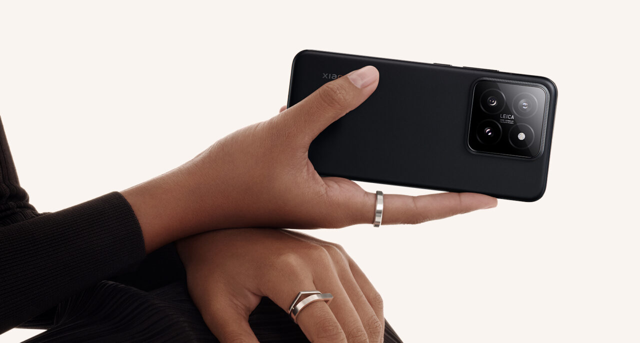 Czarna tylna część smartfona z aparatem marki Leica trzymanego w ręku osoby na neutralnym tle.