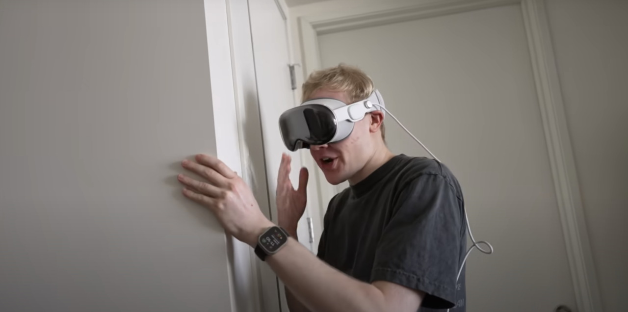 Młody mężczyzna w goglach VR opierający się o ścianę w pokoju.