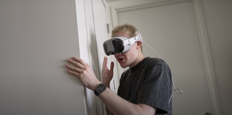 Młody mężczyzna w goglach Apple Vision Pro opierający się o ścianę w pokoju.
