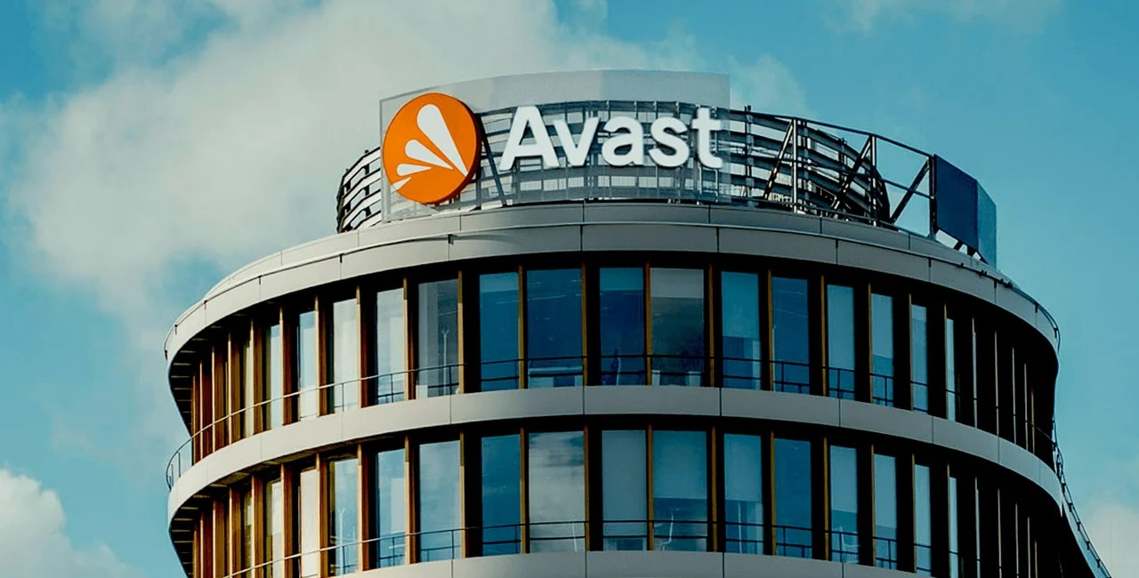 Siedziba firmy Avast, nowoczesny budynek z okrągłą, szklano-metalową fasadą i dużym logo na szczycie, na tle niebieskiego nieba z pojedynczymi chmurami.