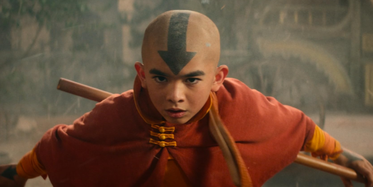 Avatar: Ostatni Władca Wiatru. Chłopiec w pomarańczowej szacie z symbolem strzałki na głowie trzyma laskę bojową w dynamicznej pozie.