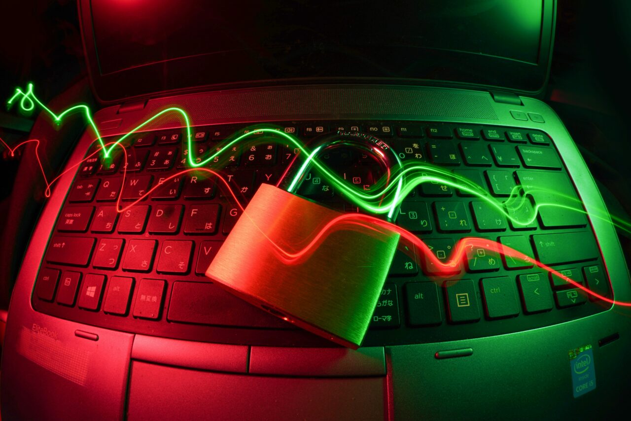 Laptop z klawiaturą podświetlaną czerwonymi i zielonymi światłami LED z nałożonym na niego kłódkiem, tworząc efekt światłowodowy i zapewniając bezpieczeństwo w sieci.