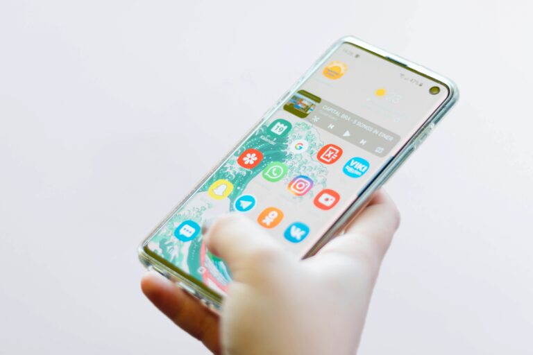 Osoba trzymająca smartfona z ekranem wyświetlającym kolorowe ikony aplikacji na jasnym tle.