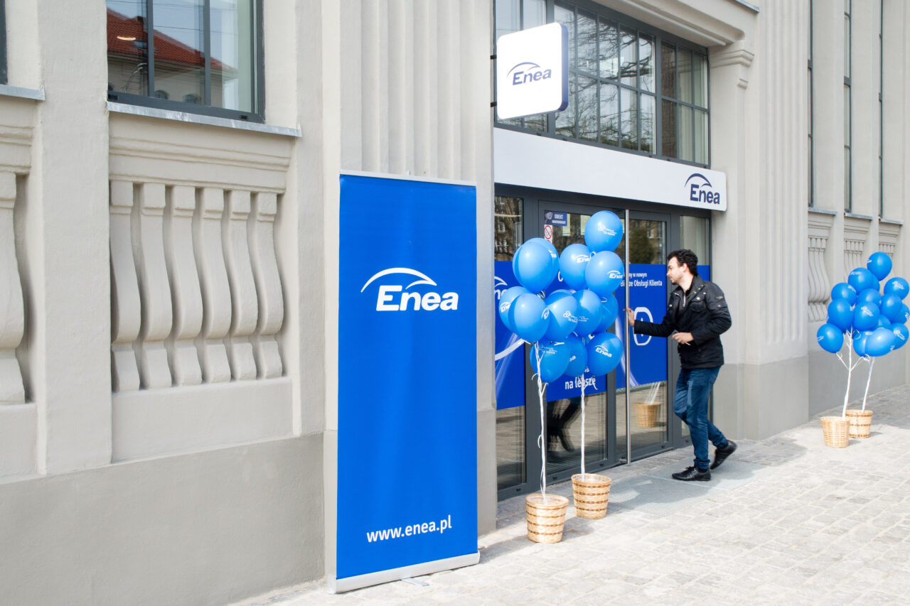 Wejście do biura firmy Enea ozdobione niebieskimi balonami, z mężczyzną wychodzącym z budynku.