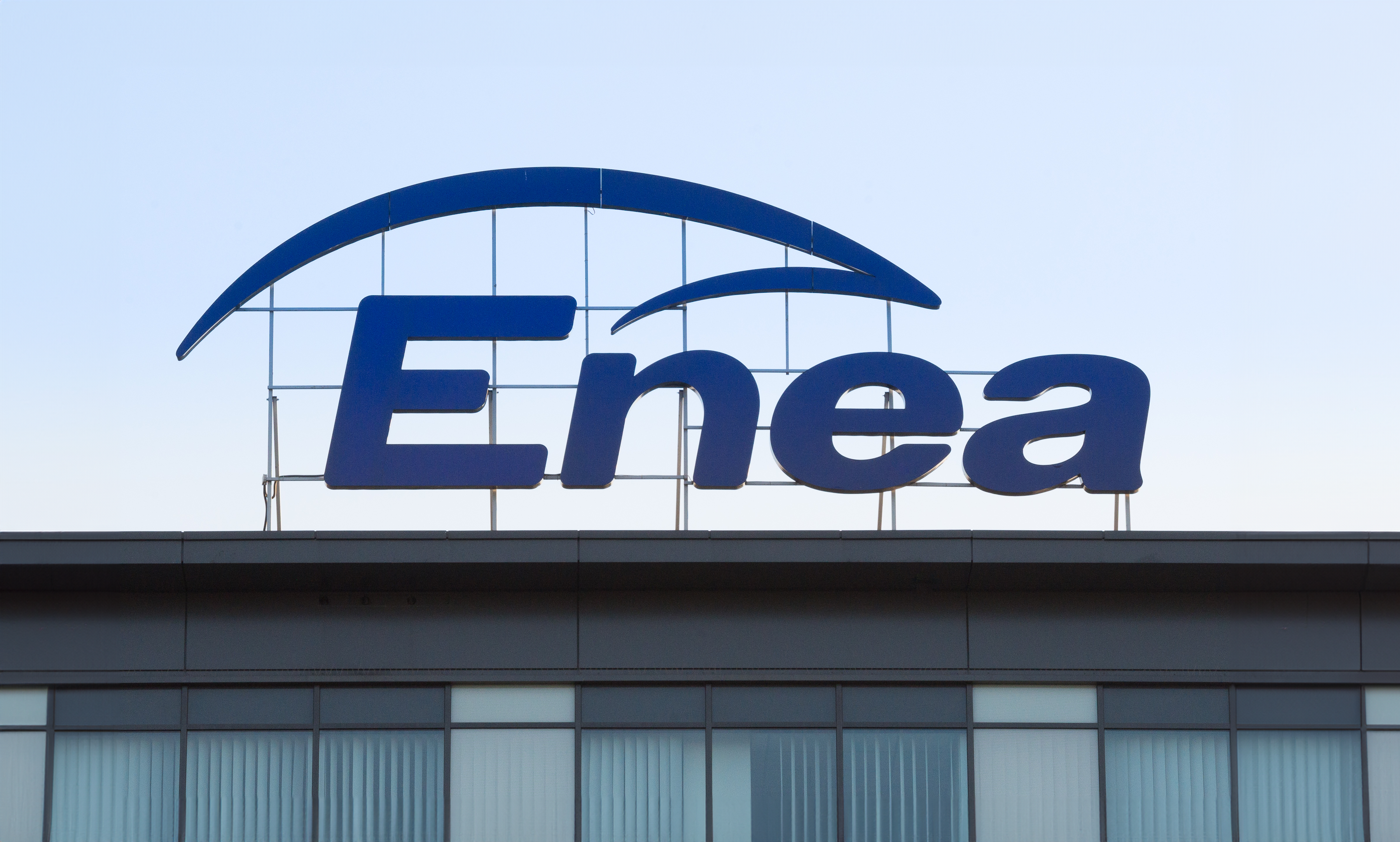 Logo firmy Enea na budynku przy niebieskim niebie.