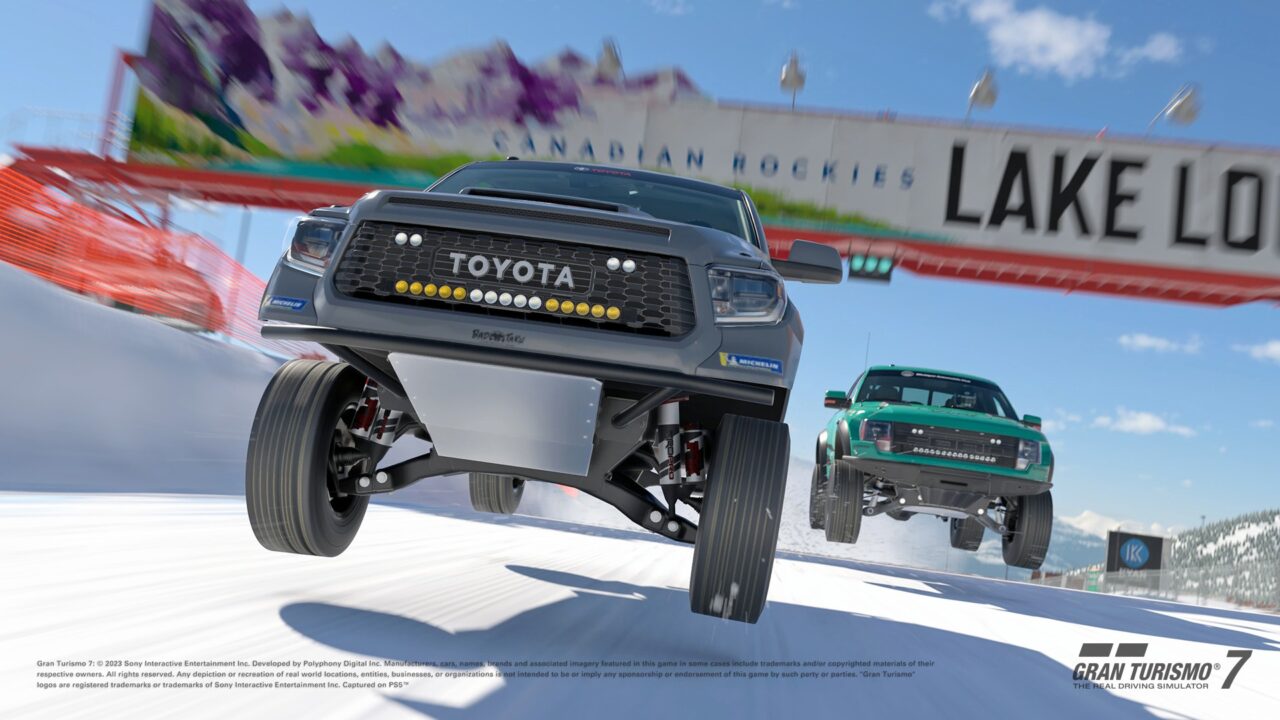 Grafika przedstawiająca dwa samochody z gry Gran Turismo 7 terenowe marki Toyota i Ford, które ścigają się na zaśnieżonej trasie w grze Gran Turismo 7, z widocznym tłem kanadyjskich Gór Skalistych i napisem "Lake Louise".