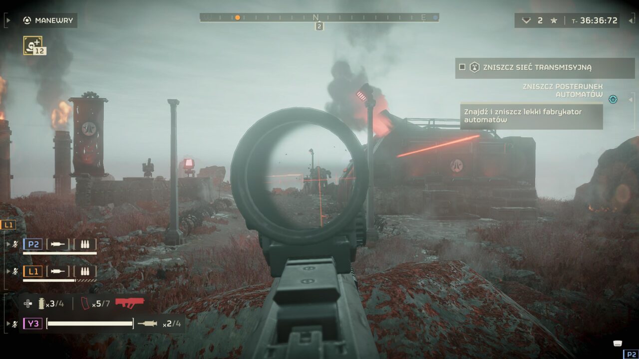 Widok z pierwszej osoby w grze wideo Helldivers 2 z celownikiem skierowanym na postapokaliptyczny, przemysłowy krajobraz z unoszącymi się kłębami dymu i czerwonymi laserami. Na ekranie widoczne są elementy interfejsu użytkownika, takie jak wskaźniki amunicji, zadania i kompas.