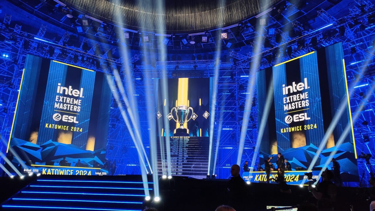 Scena turnieju Intel Extreme Masters w Katowicach z oświetlonym pucharem na podium, dużymi wyświetlaczami i efektami świetlnymi.