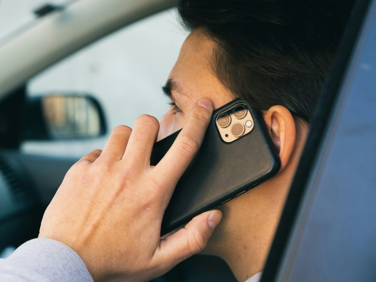 Mężczyzna trzymający przy uchu czarny smartfon, rozmawiając w samochodzie.