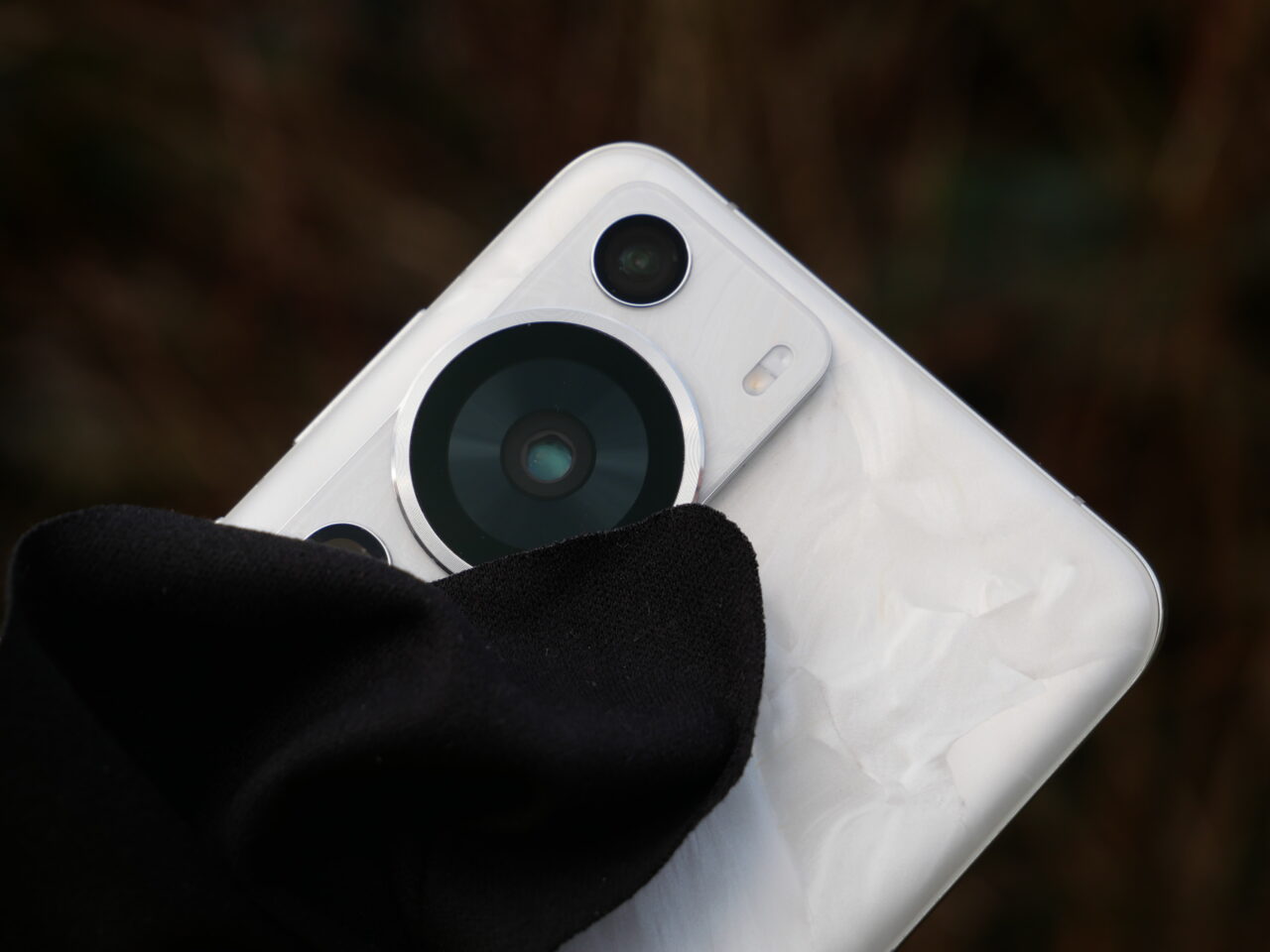 Tylny aparat fotograficzny smartfona z trzema obiektywami i lampą błyskową, czyścimy bawełnianą ściereczką, na nieostro tło.