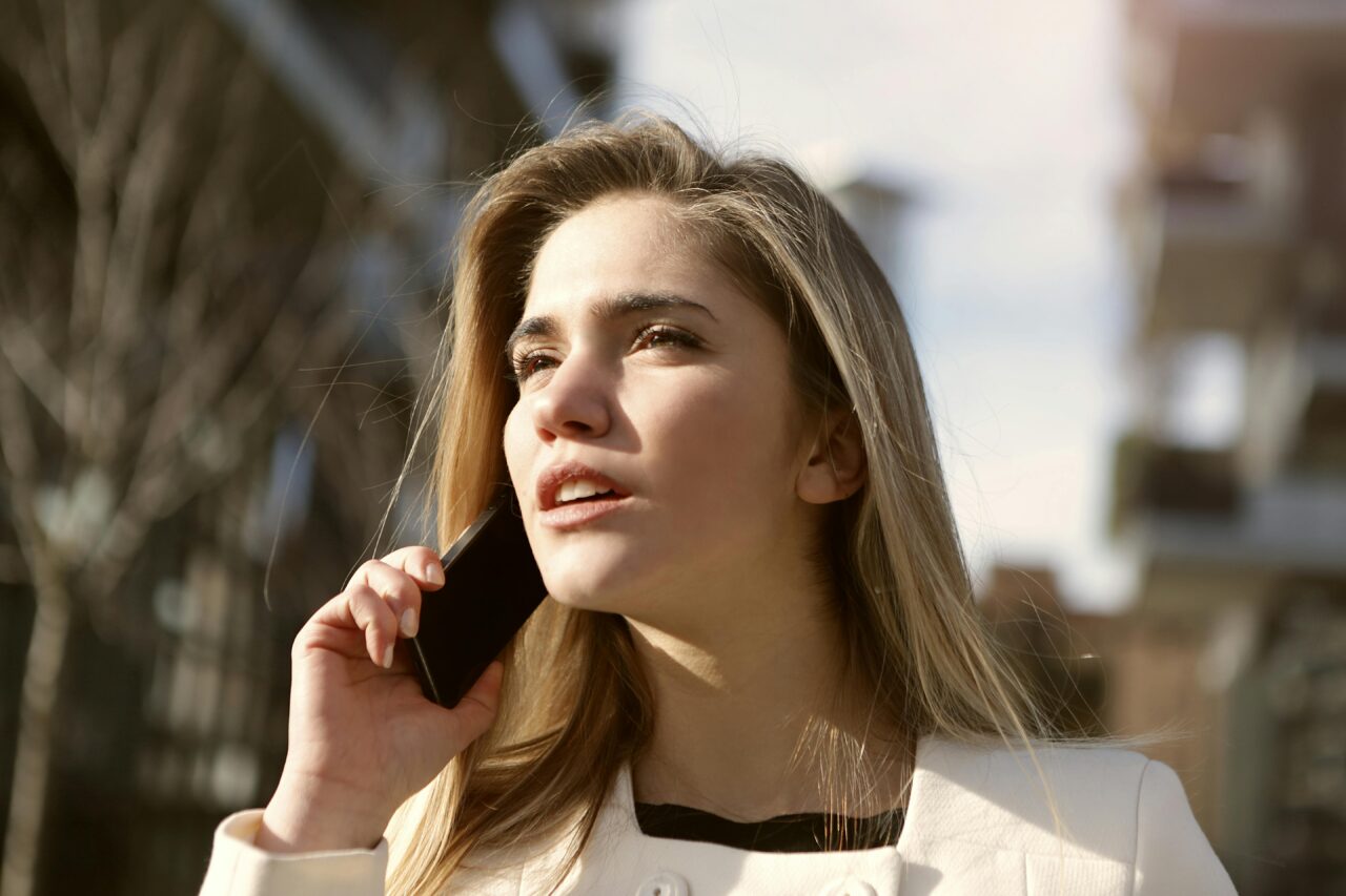 Młoda kobieta mająca abonament z telefonem w orange rozmawia przez telefon komórkowy na zewnątrz w słoneczny dzień.